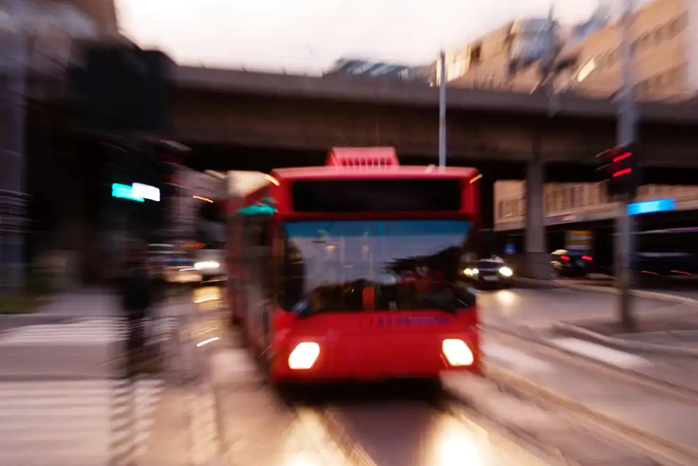 A red bus driving down a city street, surrounded by tall buildings and bustling traffic.